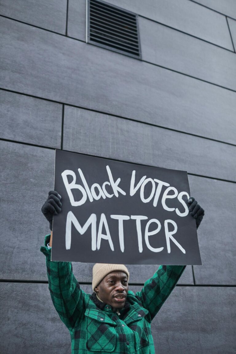 A man in a beanie holds a Black Votes Matter sign during a street protest.